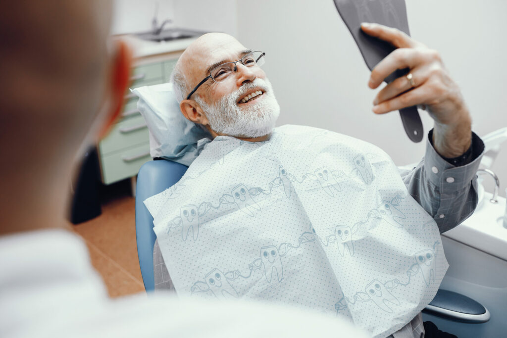 elderly man with glasses smiling in the mirror at dentist